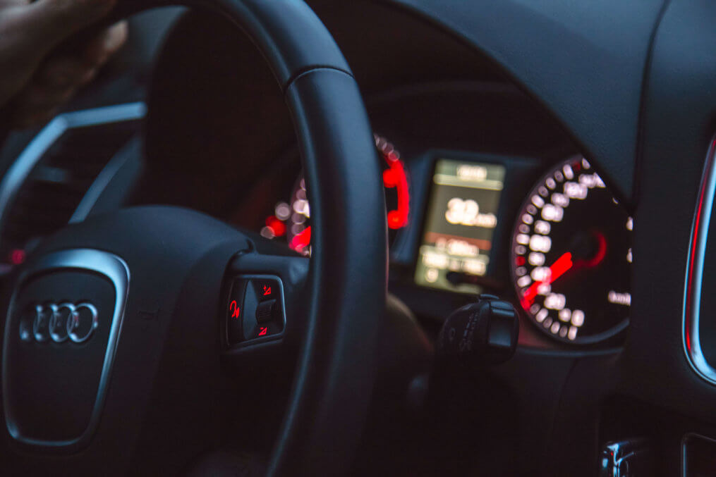 Imagem com foco no volante e painel aceso de um carro, funcionando à base de baterias automotivas.