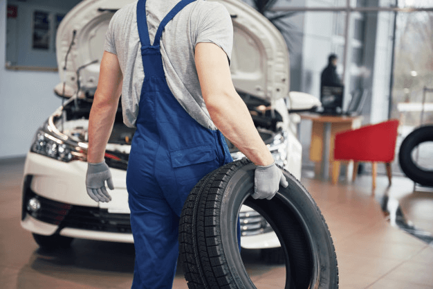Homem em pé segurando um pneu na frente de um carro fazendo manutenção na junta homocinética