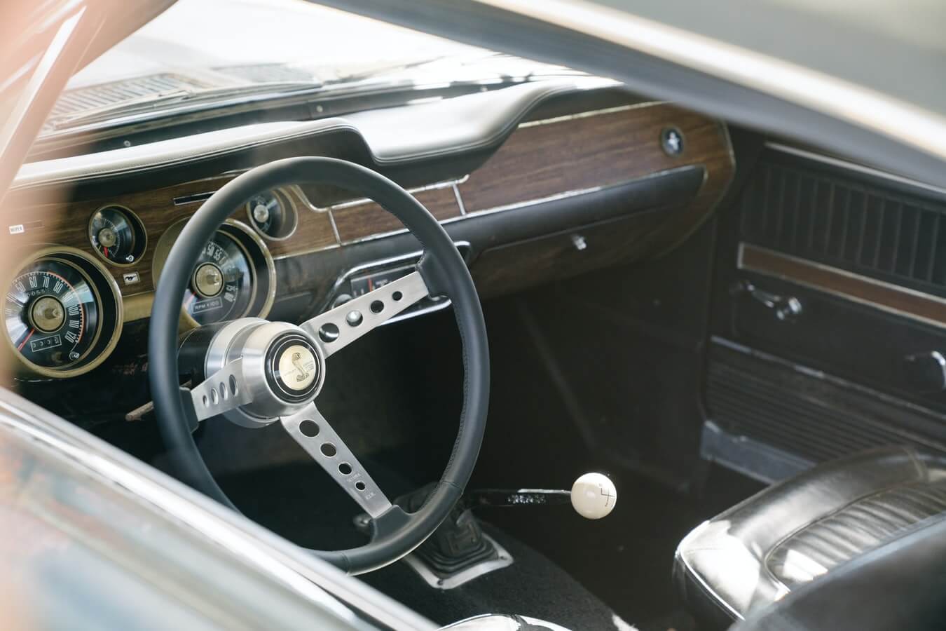 Imagem mostra parte interna de um veículo antigo, volantes, bancos e marcha de carro