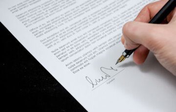 Folha de sulfite com contrato sendo assinado por uma pessoa segurando uma caneta para explicar Como obter o Certificado de Segurança Veicular